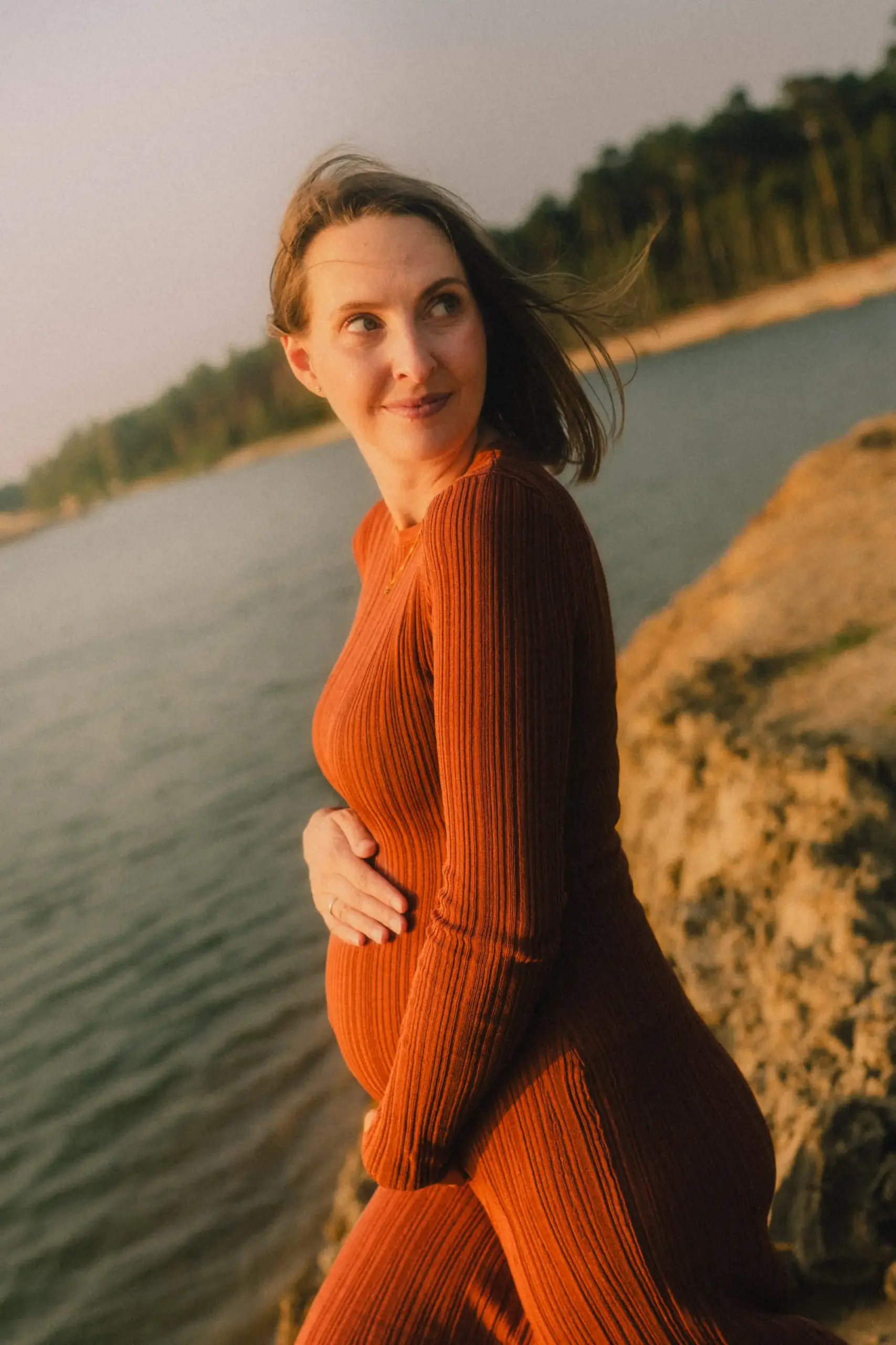 Schwangere Frau wehenden Haaren und Rostroten Kleid am See