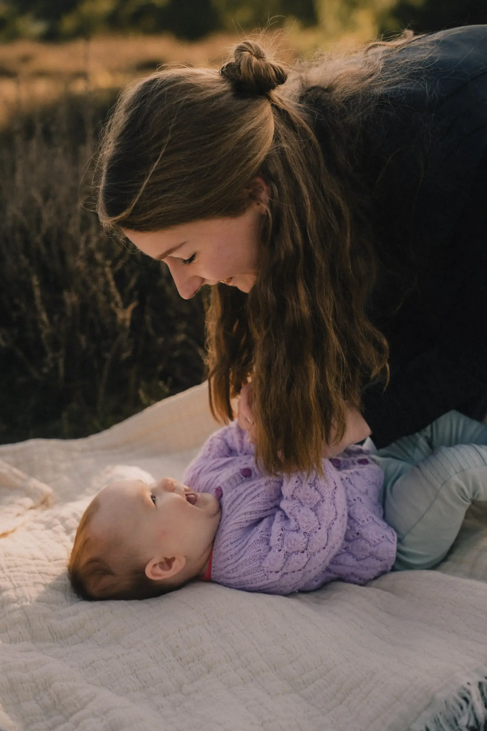Mutter und Baby spielen auf einer Picknickdecke im Sonnenuntergang
